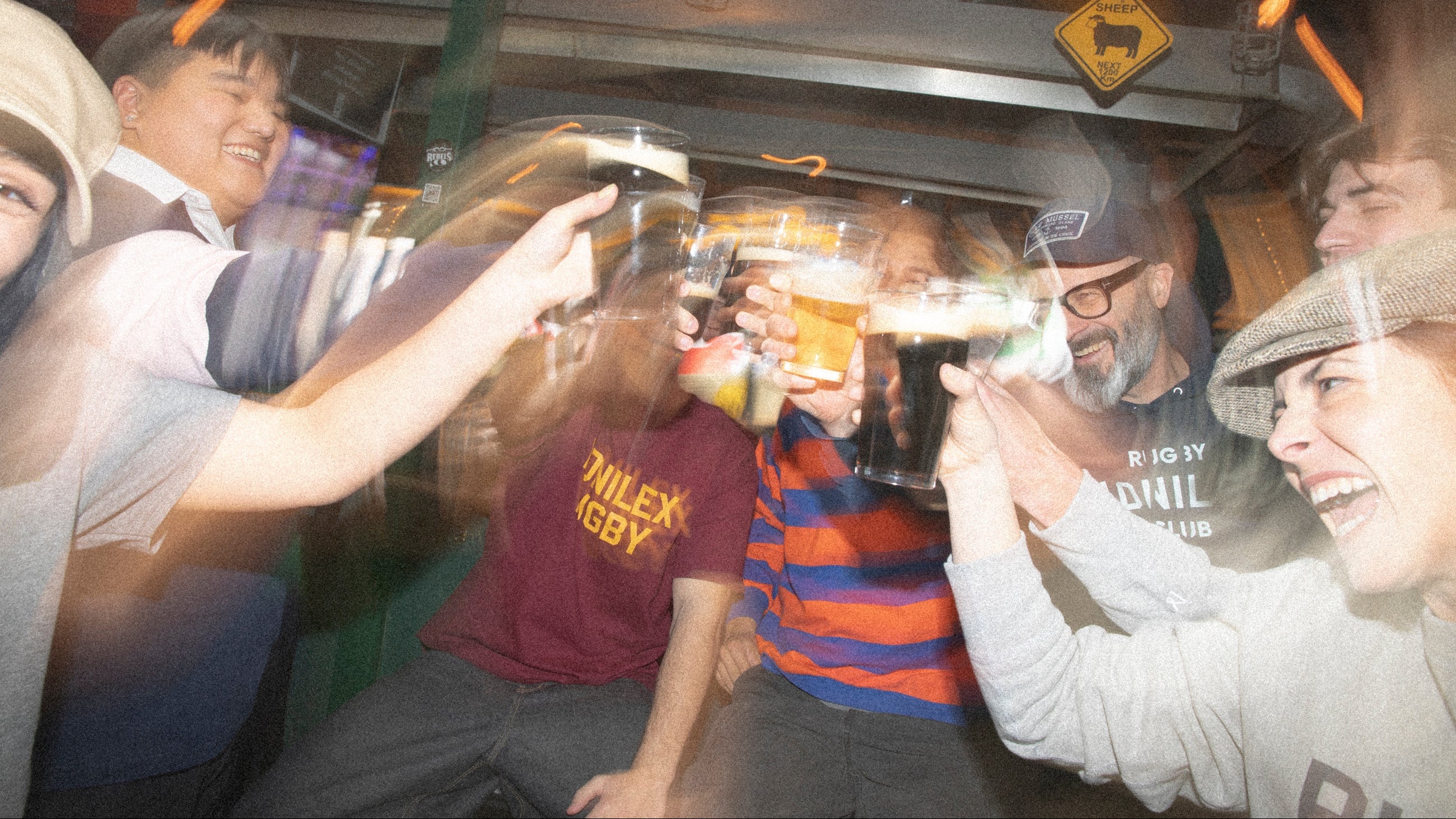 Group of people inside a pub, raising glasses in a celebratory manner.
